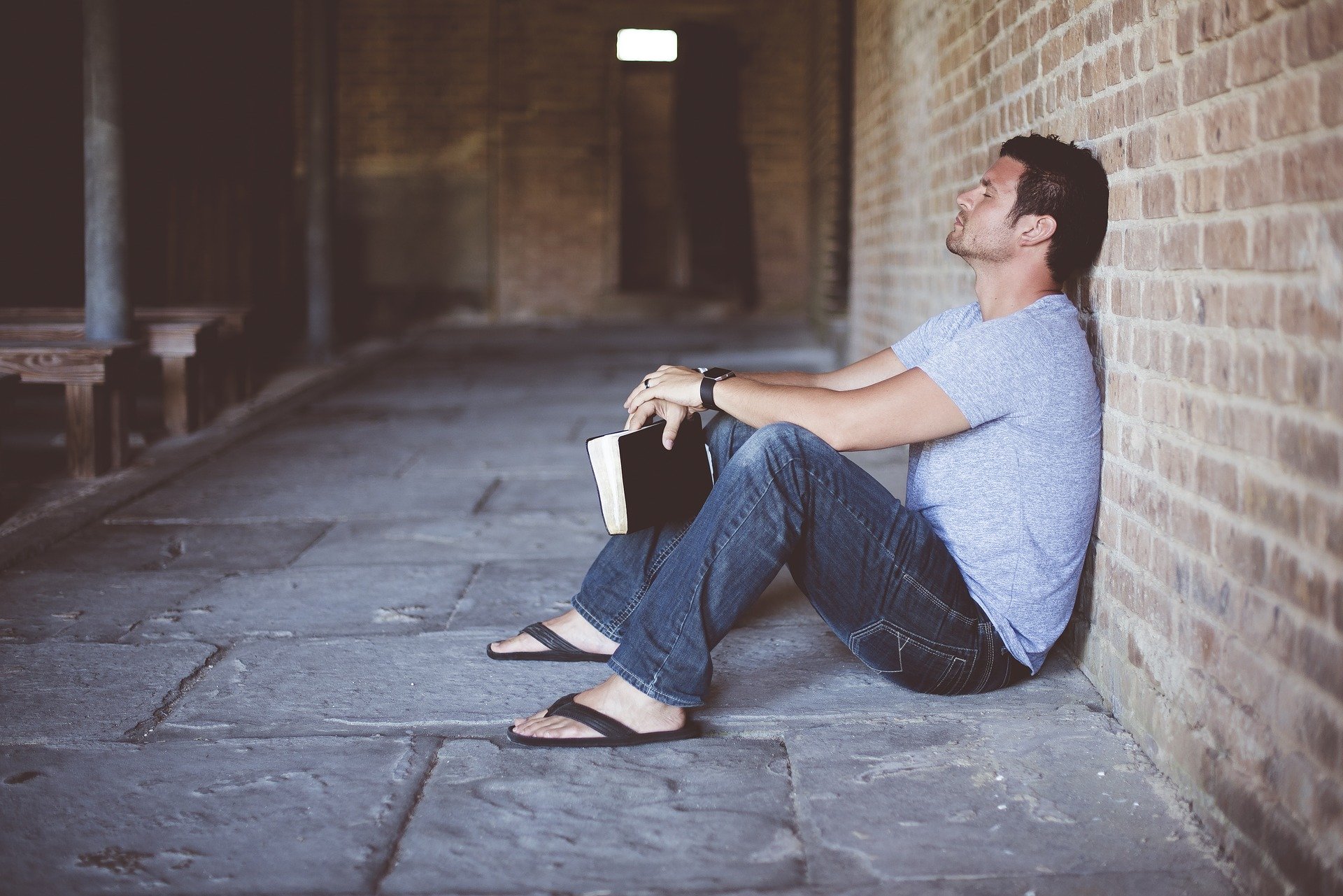 A man leans against a wall holding a book