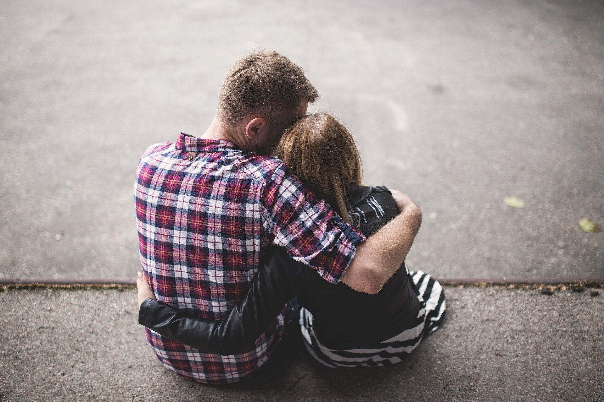 A young couple sit with arms around each other