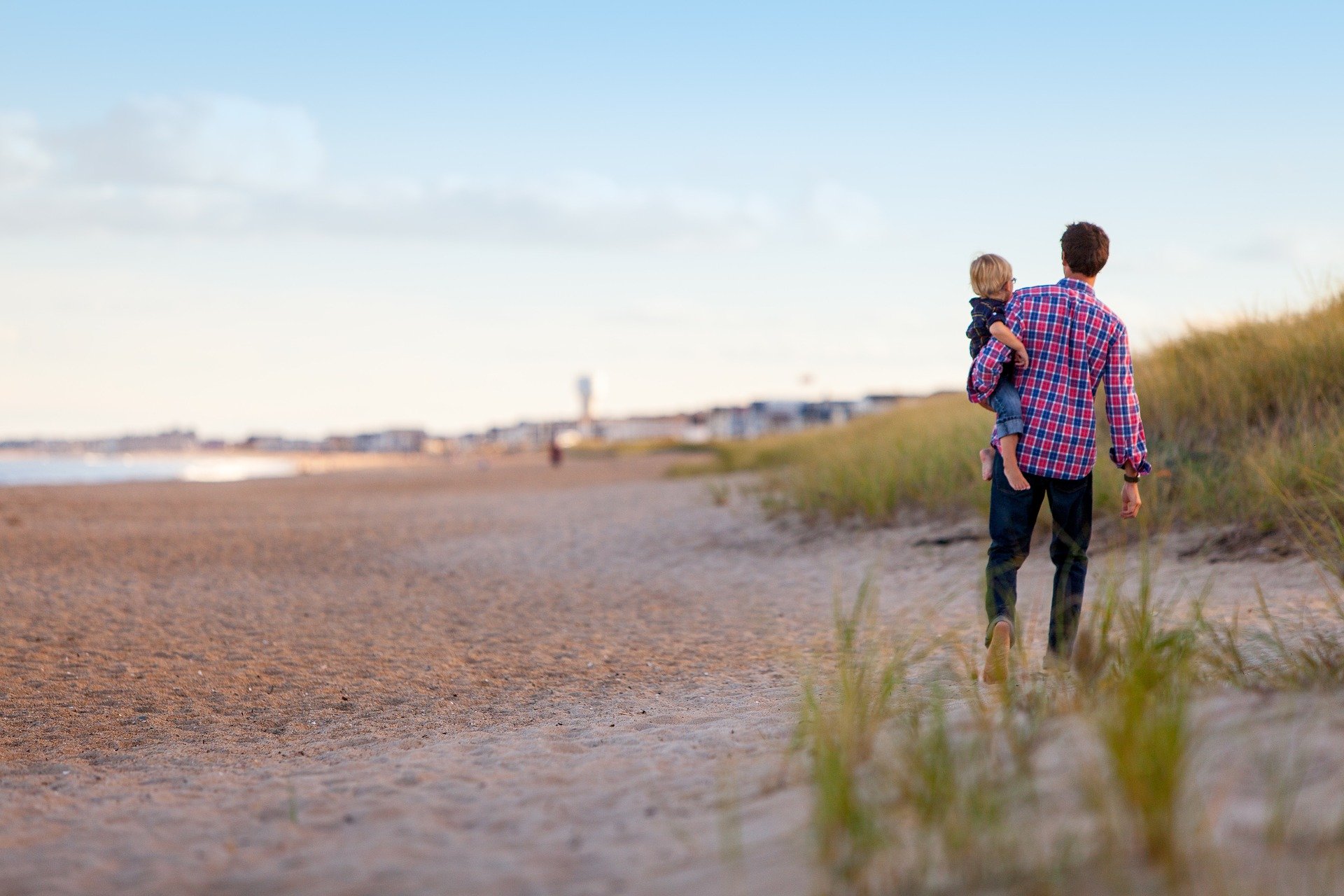 A man carries a young boy down a beach