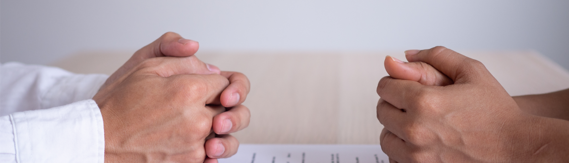 Two pairs of hands rest amicably on top of a divorce settlement document, alongside a pen and their wedding rings.