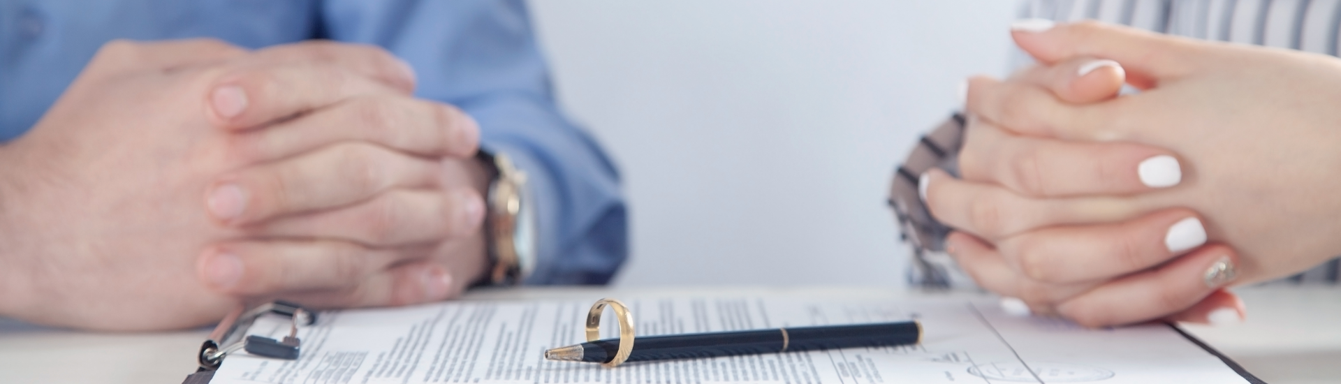 A couple sign paperwork with a wedding ring on the table.