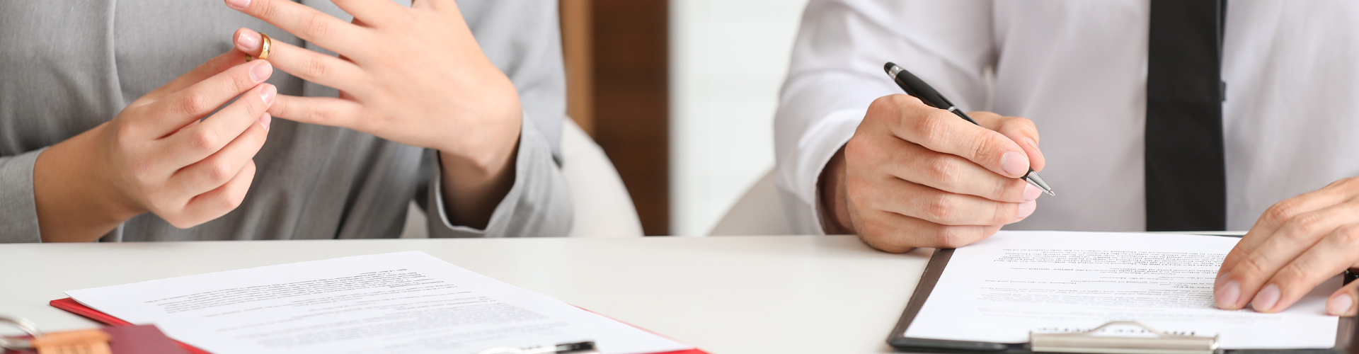 A couple sign paperwork with a wedding ring being removed.